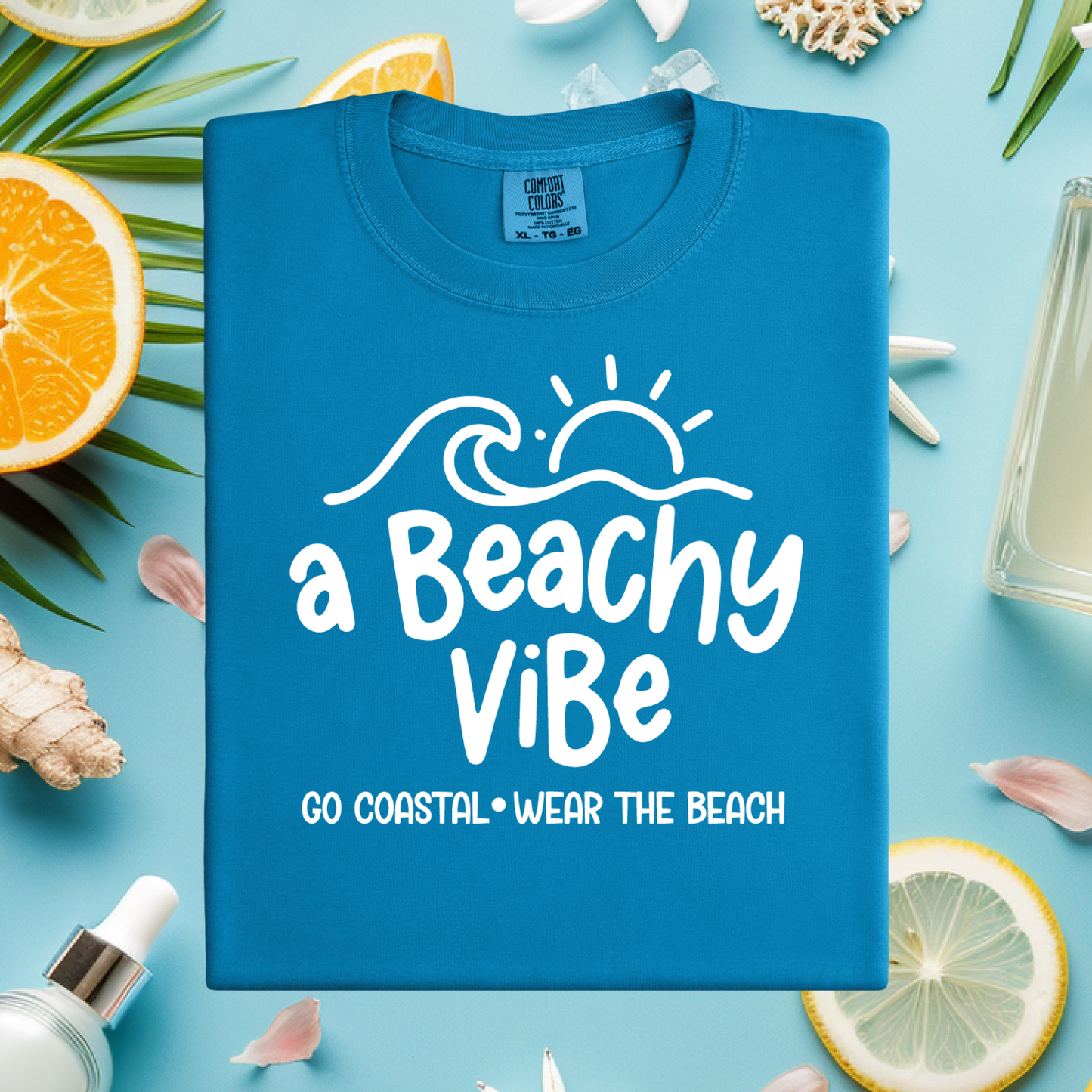 Blue t-shirt with 'a Beachy Vibe' text on a beach-themed background with lemons, oranges, and shells.
