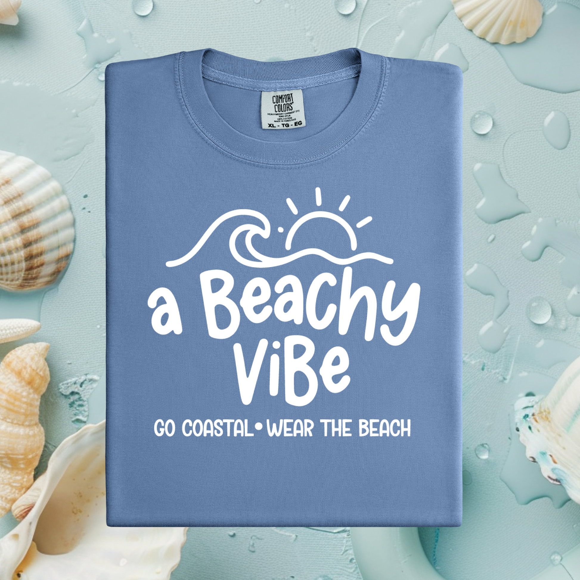 Blue t-shirt with 'a Beachy Vibe' text on a textured surface with shells.