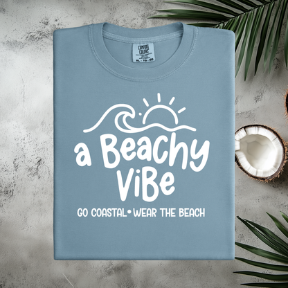 Blue t-shirt with 'a Beachy ViBé' text on a textured surface with coconut and leaves.