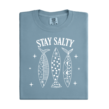Folded blue t-shirt with 'Stay Salty' text and fish illustrations on a white background