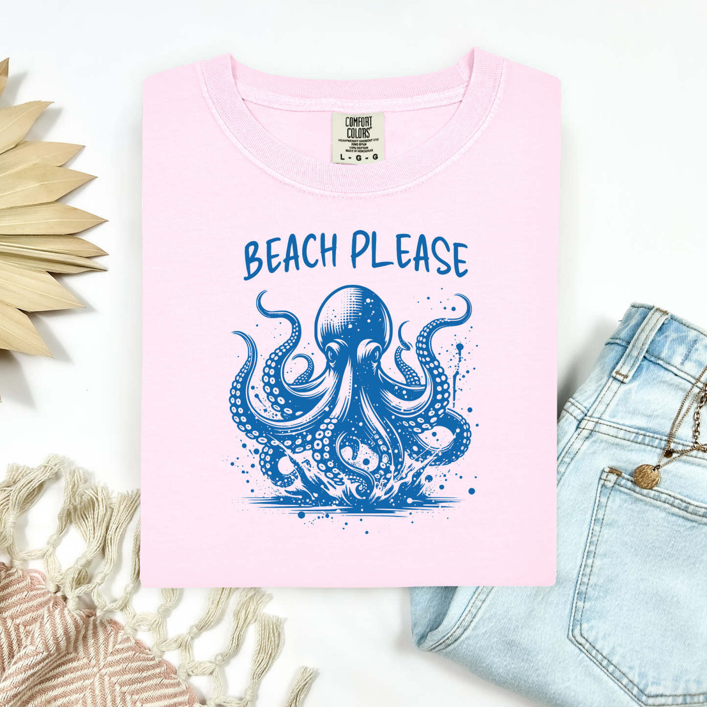 Comfort Colors 1717 "Beach Please" t shirt with a octopus  jumping in water in one color graphic. Picture on a flay lay mockup with pair of blue jeans and blanket and a wicker sun shaped accessory.