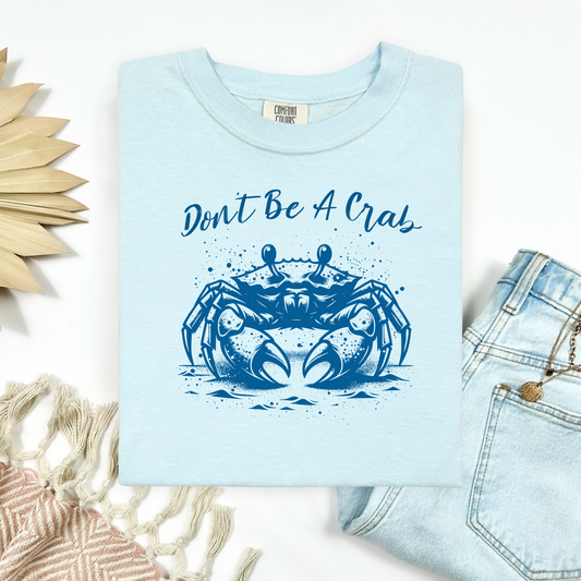 Comfort Colors 1717 "Don't Be A Crab" t shirt with a crab walking on the beach graphics in one color graphic. Picture on a flay lay mockup with pair of blue jeans and blanket and a wicker sun shaped accessory.
