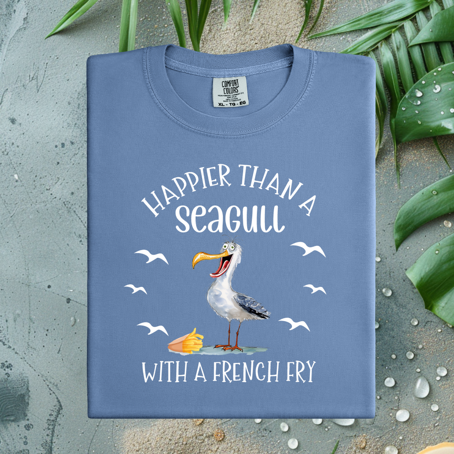 Blue t-shirt with a seagull graphic and text on a textured surface with leaves.