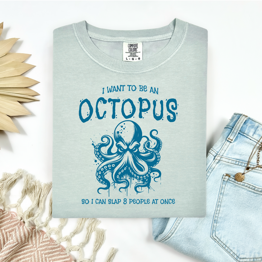 Comfort Colors 1717 "I Want To Be On Octopus So I Can Slap 8 People At Once" t shirt with an angry octopus one color graphic. Picture on a flay lay mockup with pair of blue jeans and blanket and a wicker sun shaped accessory.
