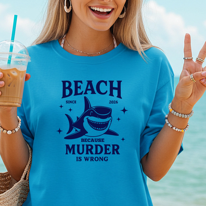 Comfort Colors t-shirt featuring a blue cartoon shark illustration with the humorous text “Beach Because Murder Is Wrong” and “Since 2026.” The design includes sparkling star accents for a fun coastal look. This unisex garment-dyed tee offers soft, vintage-style cotton and a relaxed fit, perfect for beach lovers, humor fans, and anyone who enjoys playful ocean-themed graphic shirts.