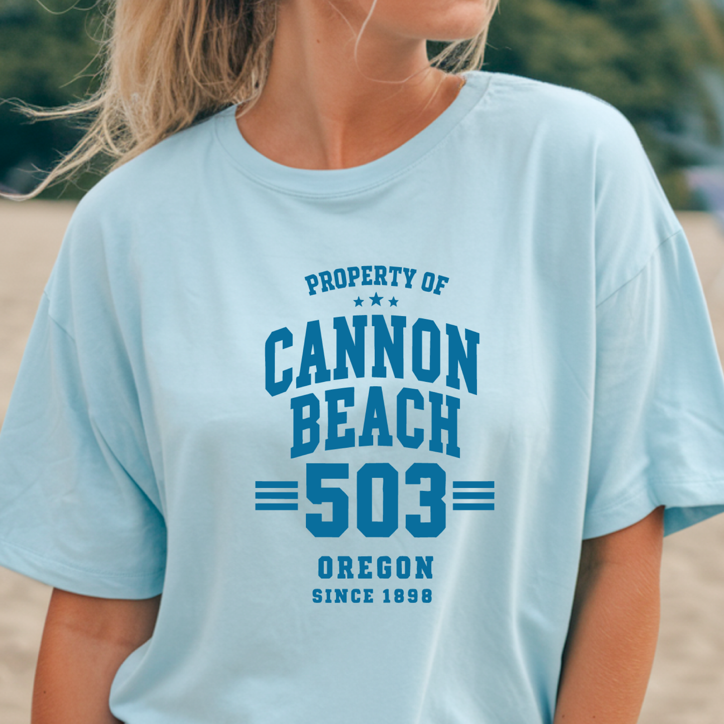 Light blue t-shirt with 'Cannon Beach 503' text worn by a person outdoors.
