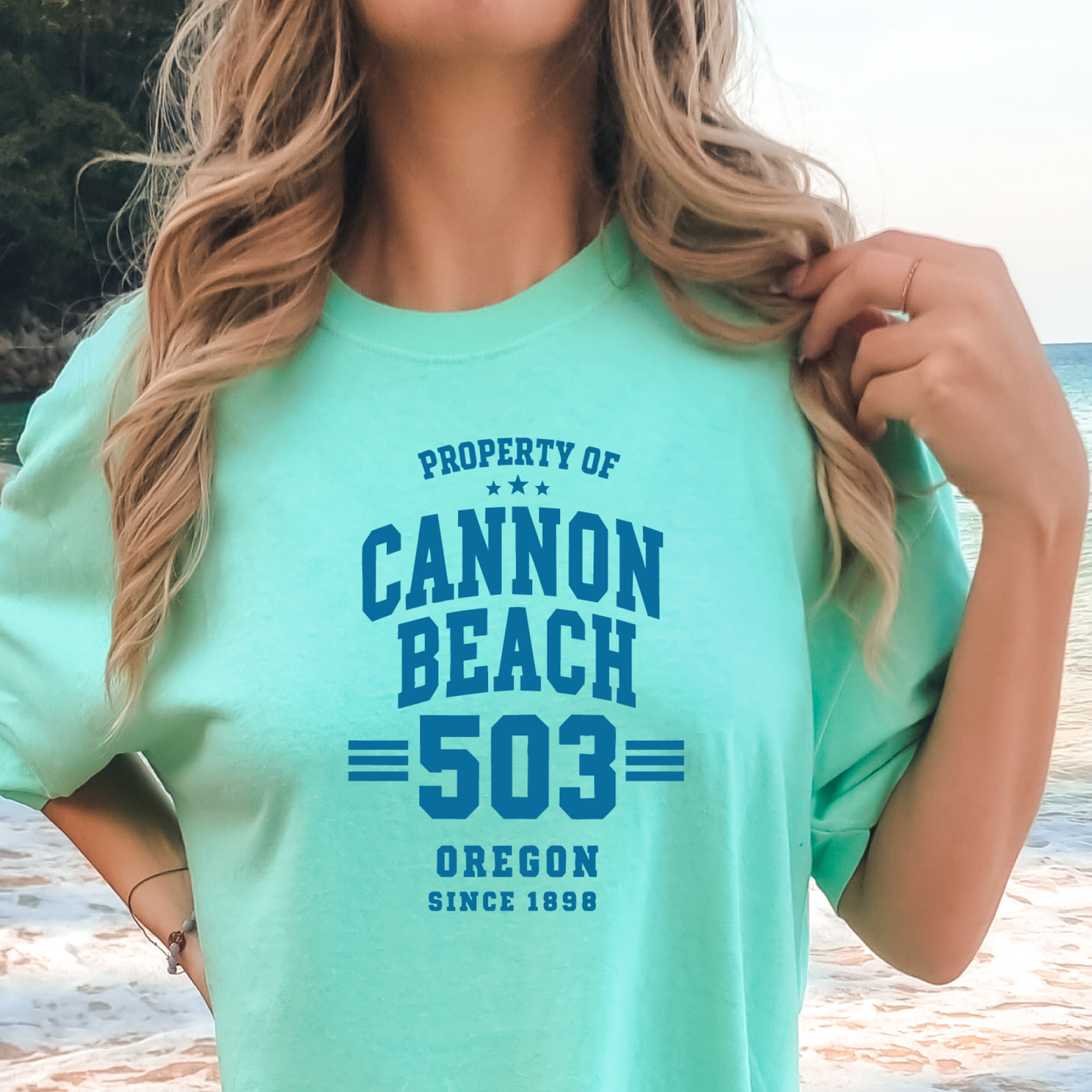Person wearing a teal t-shirt with 'Cannon Beach 503 Oregon' text at the beach.