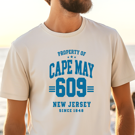 Person wearing a t-shirt with 'Property of Cape May 609 New Jersey Since 1848' text on a beach.