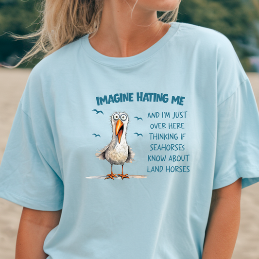 Person wearing a light blue t-shirt with a cartoon seagull and humorous text on a beach.