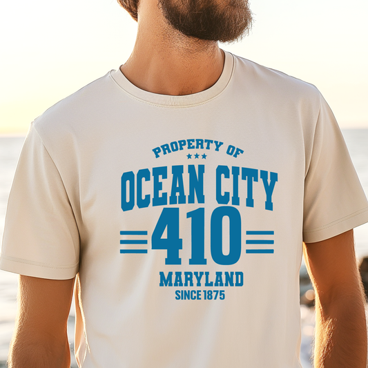Person wearing a t-shirt with 'Property of Ocean City 410 Maryland Since 1875' text on a beach.