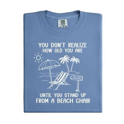 Folded blue t-shirt with beach-themed design and text on a white background