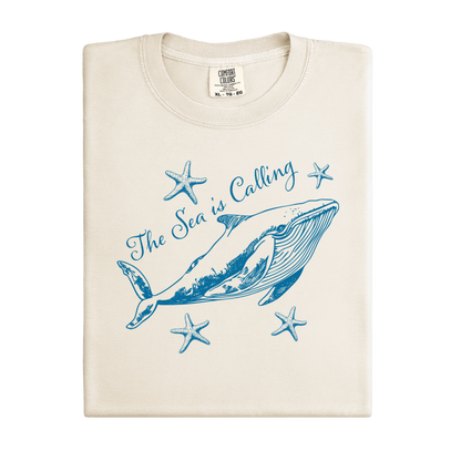 Comfort Colors t-shirt featuring a blue whale illustration surrounded by starfish and the handwritten-style text “The Sea is Calling.” The detailed marine artwork creates a calming coastal aesthetic. This unisex garment-dyed tee offers a soft vintage feel and relaxed fit, perfect for ocean lovers, beach trips, and anyone who enjoys sea-themed graphic shirts with a coastal vibe.