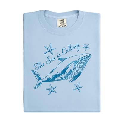 Comfort Colors t-shirt featuring a blue whale illustration surrounded by starfish and the handwritten-style text “The Sea is Calling.” The detailed marine artwork creates a calming coastal aesthetic. This unisex garment-dyed tee offers a soft vintage feel and relaxed fit, perfect for ocean lovers, beach trips, and anyone who enjoys sea-themed graphic shirts with a coastal vibe.