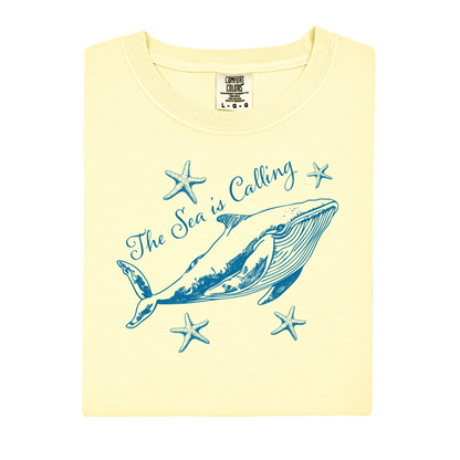 Comfort Colors t-shirt featuring a blue whale illustration surrounded by starfish and the handwritten-style text “The Sea is Calling.” The detailed marine artwork creates a calming coastal aesthetic. This unisex garment-dyed tee offers a soft vintage feel and relaxed fit, perfect for ocean lovers, beach trips, and anyone who enjoys sea-themed graphic shirts with a coastal vibe.