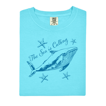 Comfort Colors t-shirt featuring a blue whale illustration surrounded by starfish and the handwritten-style text “The Sea is Calling.” The detailed marine artwork creates a calming coastal aesthetic. This unisex garment-dyed tee offers a soft vintage feel and relaxed fit, perfect for ocean lovers, beach trips, and anyone who enjoys sea-themed graphic shirts with a coastal vibe.