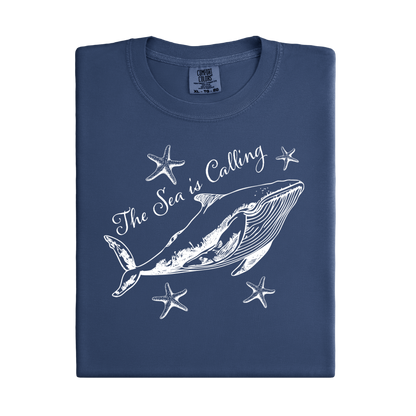 Comfort Colors t-shirt featuring a blue whale illustration surrounded by starfish and the handwritten-style text “The Sea is Calling.” The detailed marine artwork creates a calming coastal aesthetic. This unisex garment-dyed tee offers a soft vintage feel and relaxed fit, perfect for ocean lovers, beach trips, and anyone who enjoys sea-themed graphic shirts with a coastal vibe.