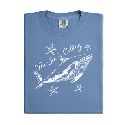 Comfort Colors t-shirt featuring a blue whale illustration surrounded by starfish and the handwritten-style text “The Sea is Calling.” The detailed marine artwork creates a calming coastal aesthetic. This unisex garment-dyed tee offers a soft vintage feel and relaxed fit, perfect for ocean lovers, beach trips, and anyone who enjoys sea-themed graphic shirts with a coastal vibe.