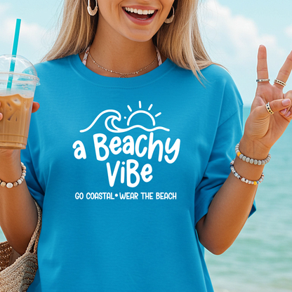Person wearing a blue 'a Beachy Vibe' shirt by the ocean