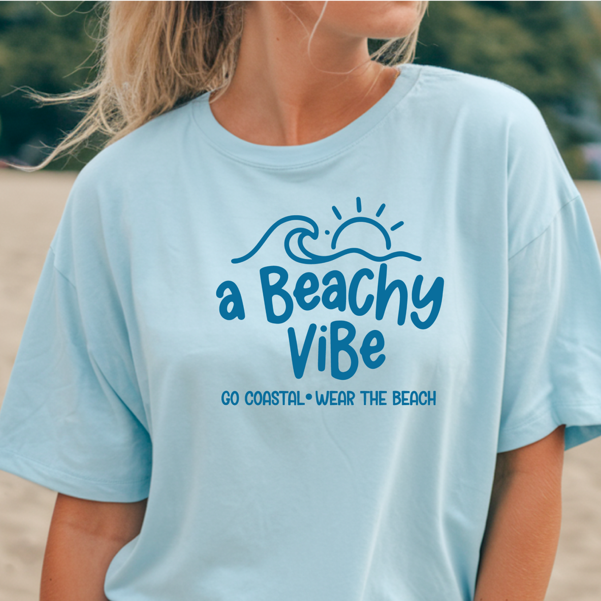 Light blue t-shirt with 'a Beachy Vibe' text and graphics worn by a person outdoors.
