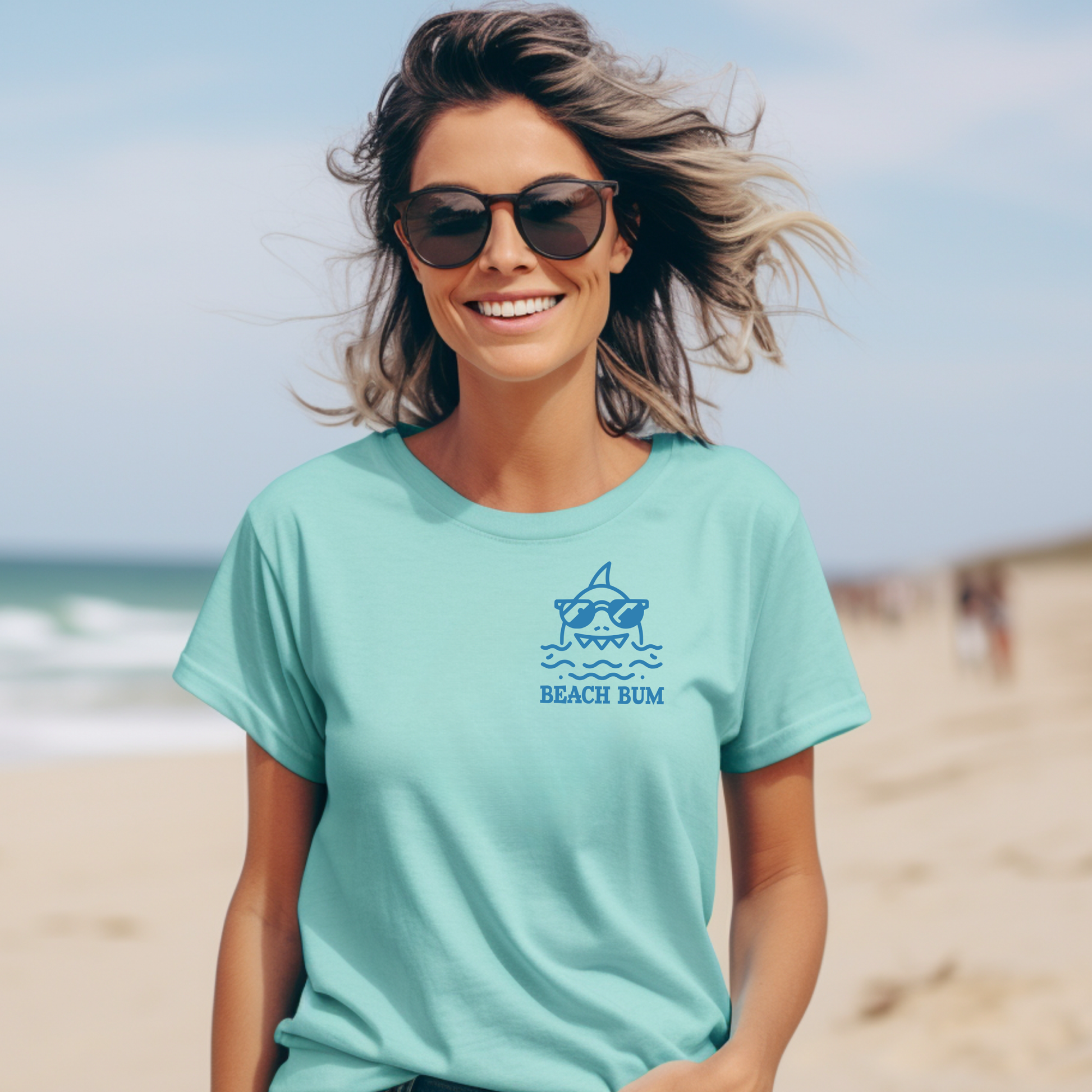 Comfort Colors 1717 "Beach Bum" t shirt with a simple line drawing of a shark wearing sunglasses in a one color graphic. Picture of a girl standing on the beach wearing a t shirt.