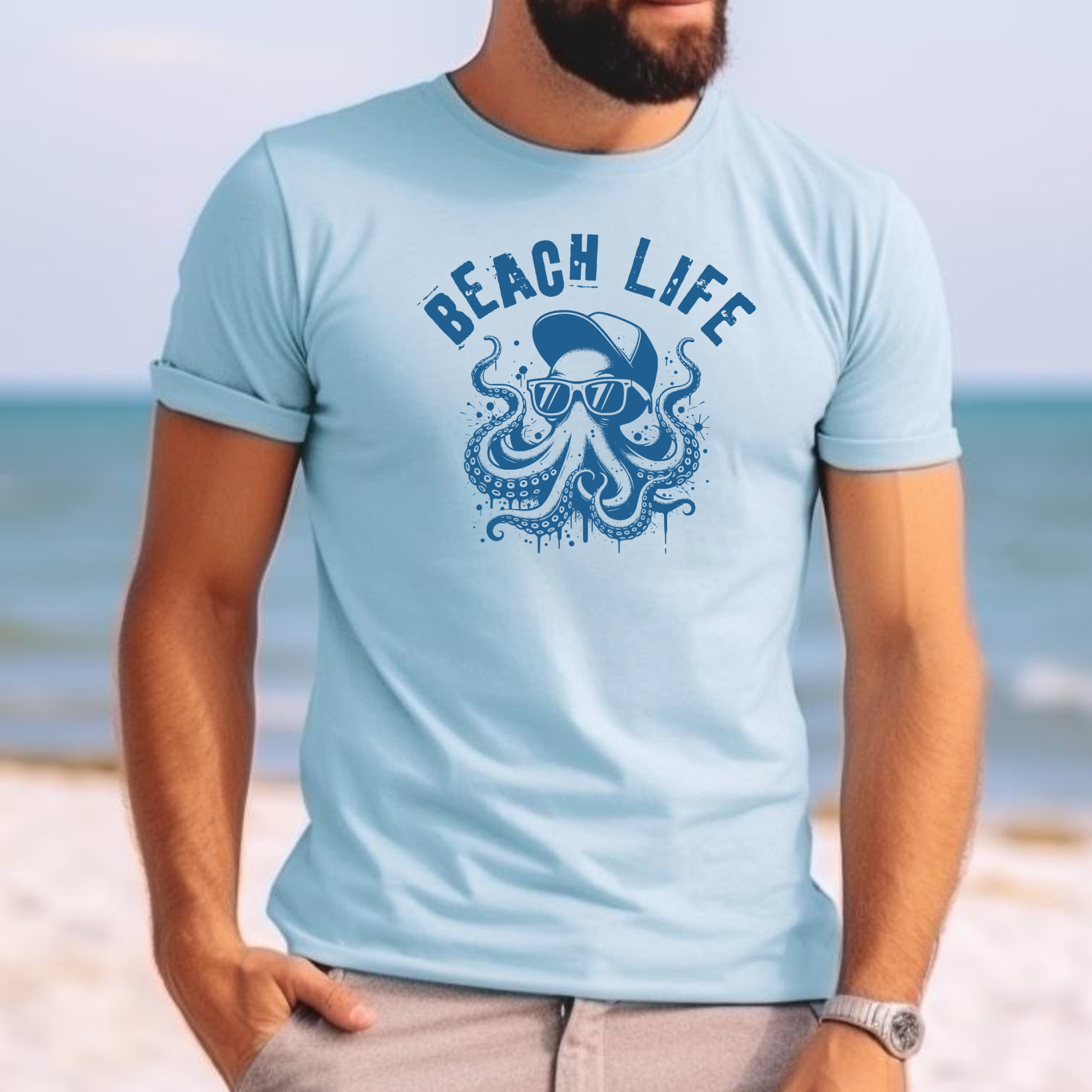 Comfort Colors 1717 "Beach Life" t shirt with a octopus with a baseball cap and sunglasses in a one color graphic. Picture of a man standing on the beach wearing a t shirt.