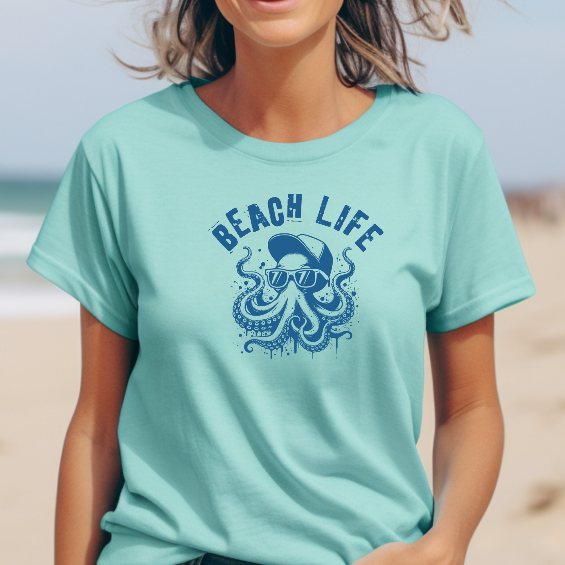 Comfort Colors 1717 "Beach Life" t shirt with a octopus with a baseball cap and sunglasses in a one color graphic. Picture of a girl  standing on the beach wearing a t shirt.