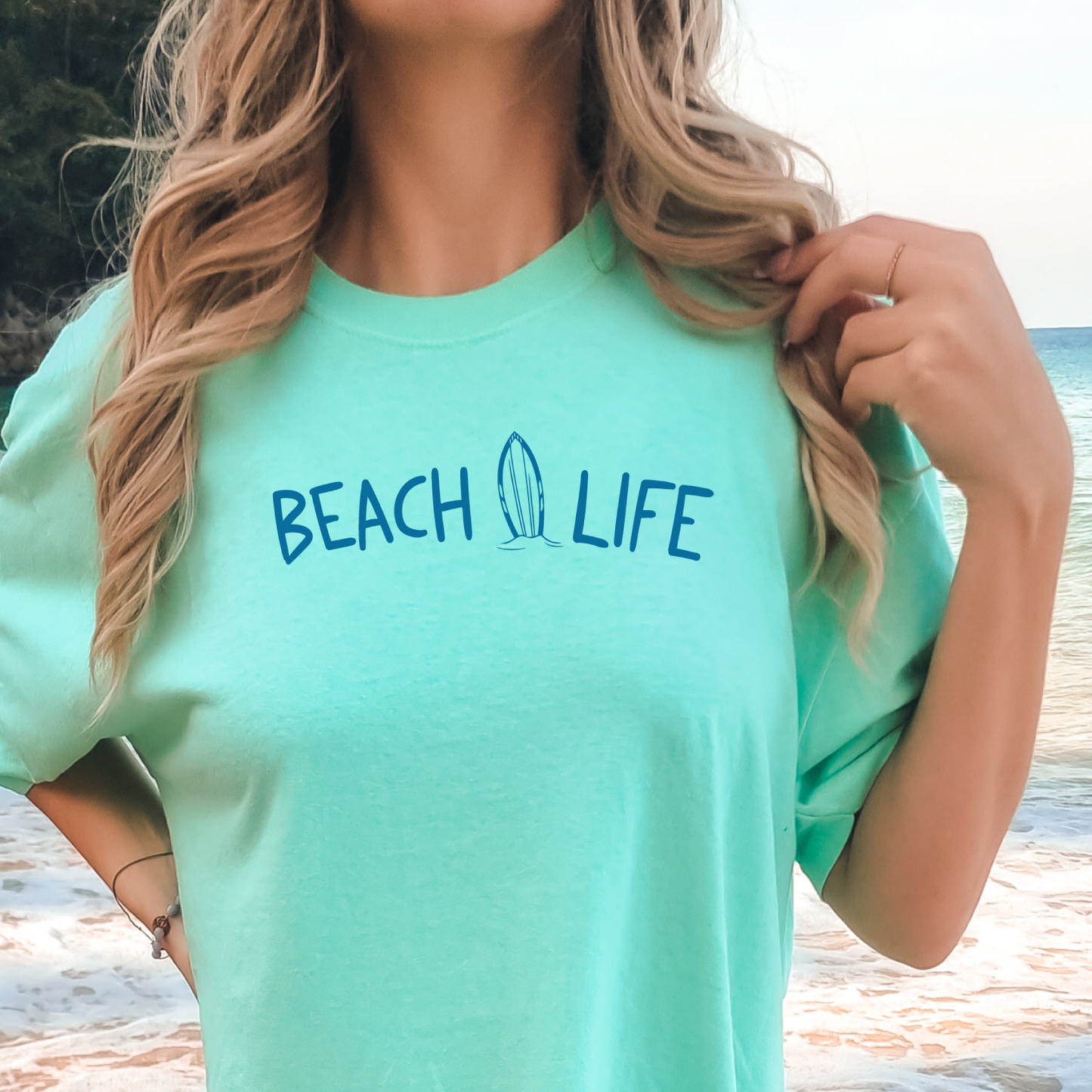 Person wearing a green 'Beach Life' t-shirt with a blurred beach background