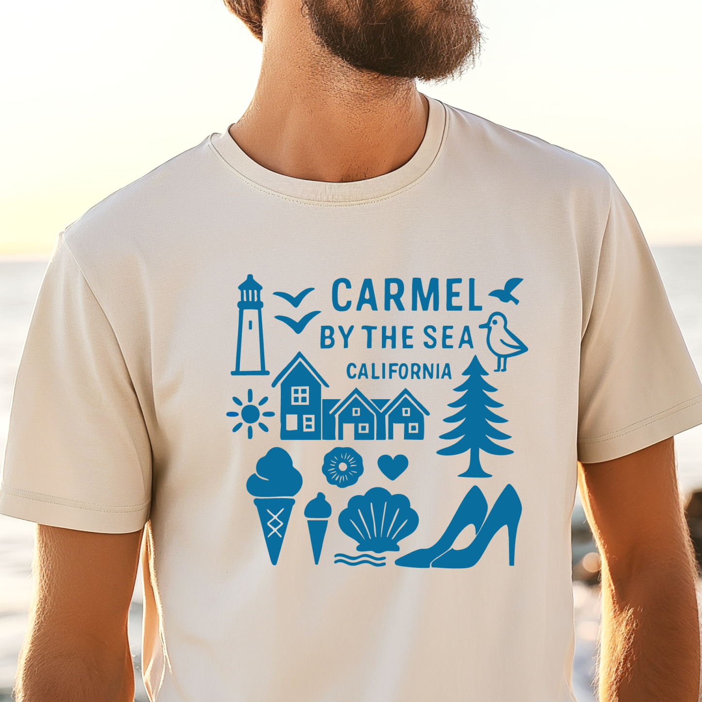 Person wearing a t-shirt with 'Carmel by the Sea, California' design on a beach.