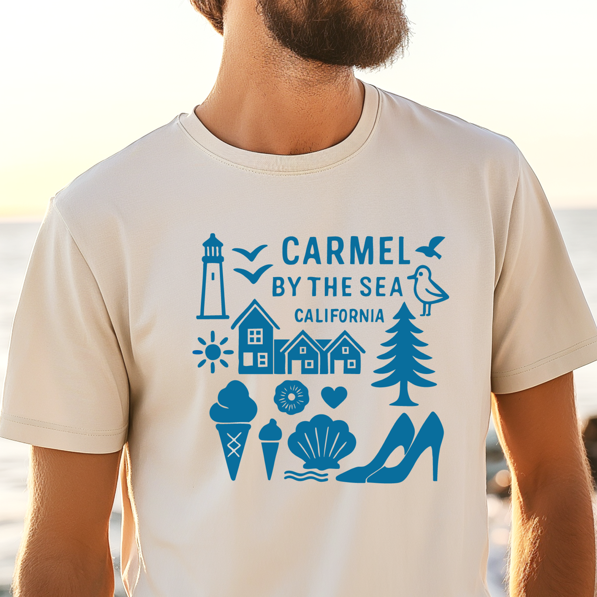 Person wearing a t-shirt with 'Carmel by the Sea, California' design on a beach.