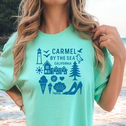 Person wearing a teal t-shirt with 'Carmel by the Sea, California' design on a beach.
