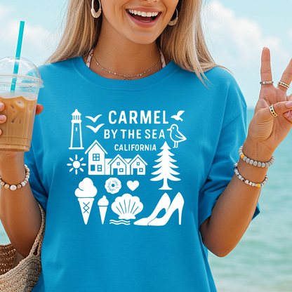 Woman wearing a blue t-shirt with 'Carmel by the Sea, California' design, holding a drink and pointing towards the sea.