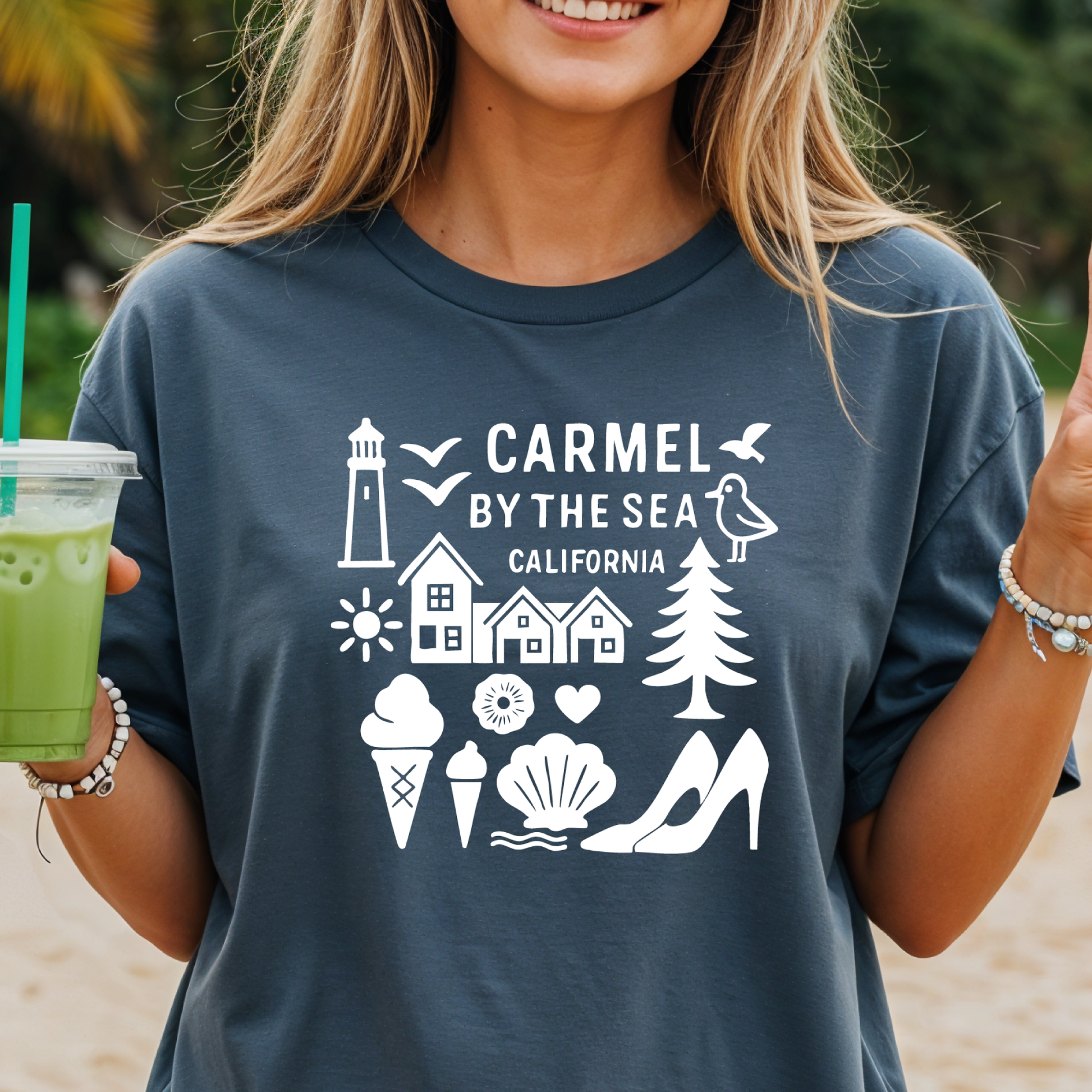Person wearing a t-shirt with 'Carmel by the Sea, California' design on a beach.