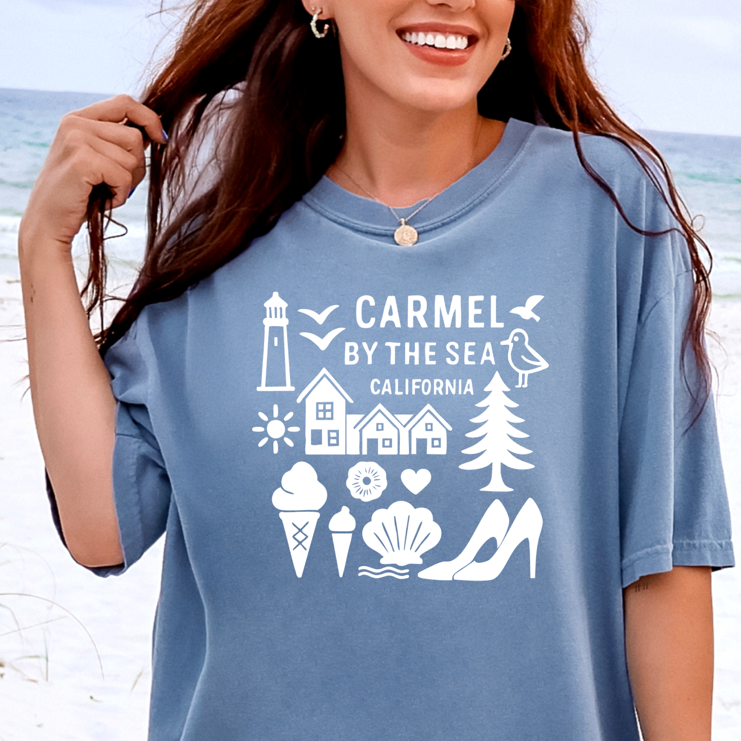 Woman wearing a blue t-shirt with 'Carmel by the Sea, California' design on a beach.