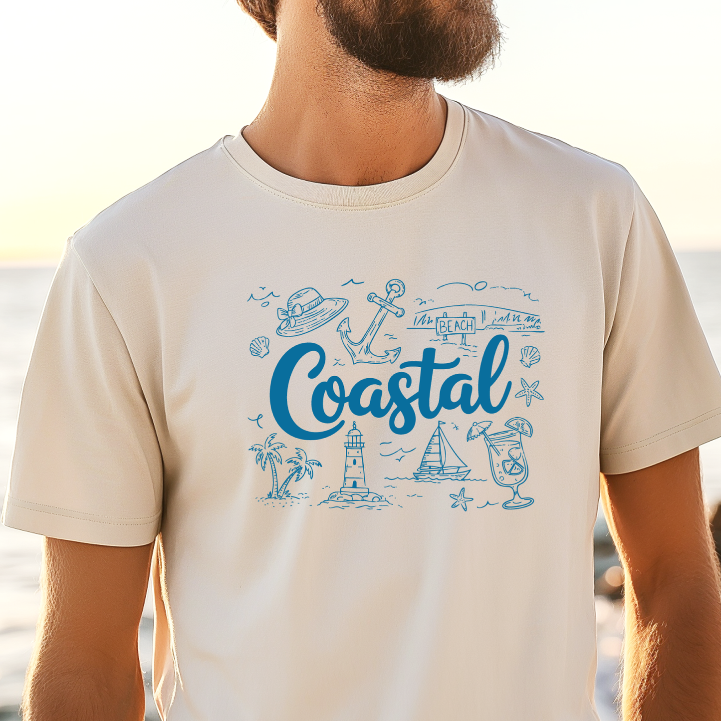 Ivory t-shirt with blue coastal graphics and text worn by a person at the beach.