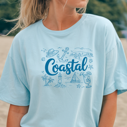 Light blue t-shirt with 'Coastal' design worn by a person on a beach.
