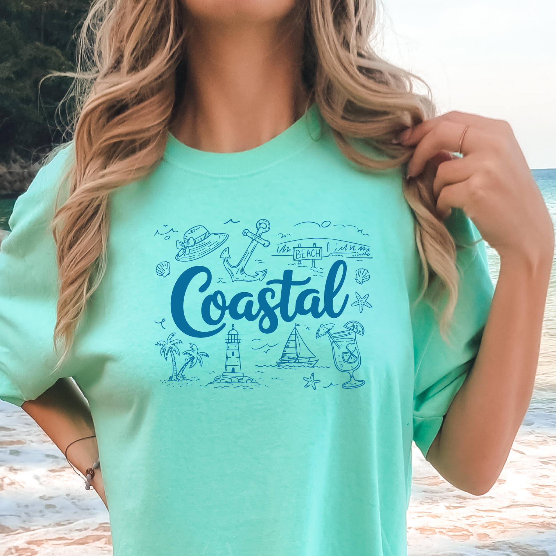 Person wearing a island reef t-shirt with 'Coastal' design on a beach