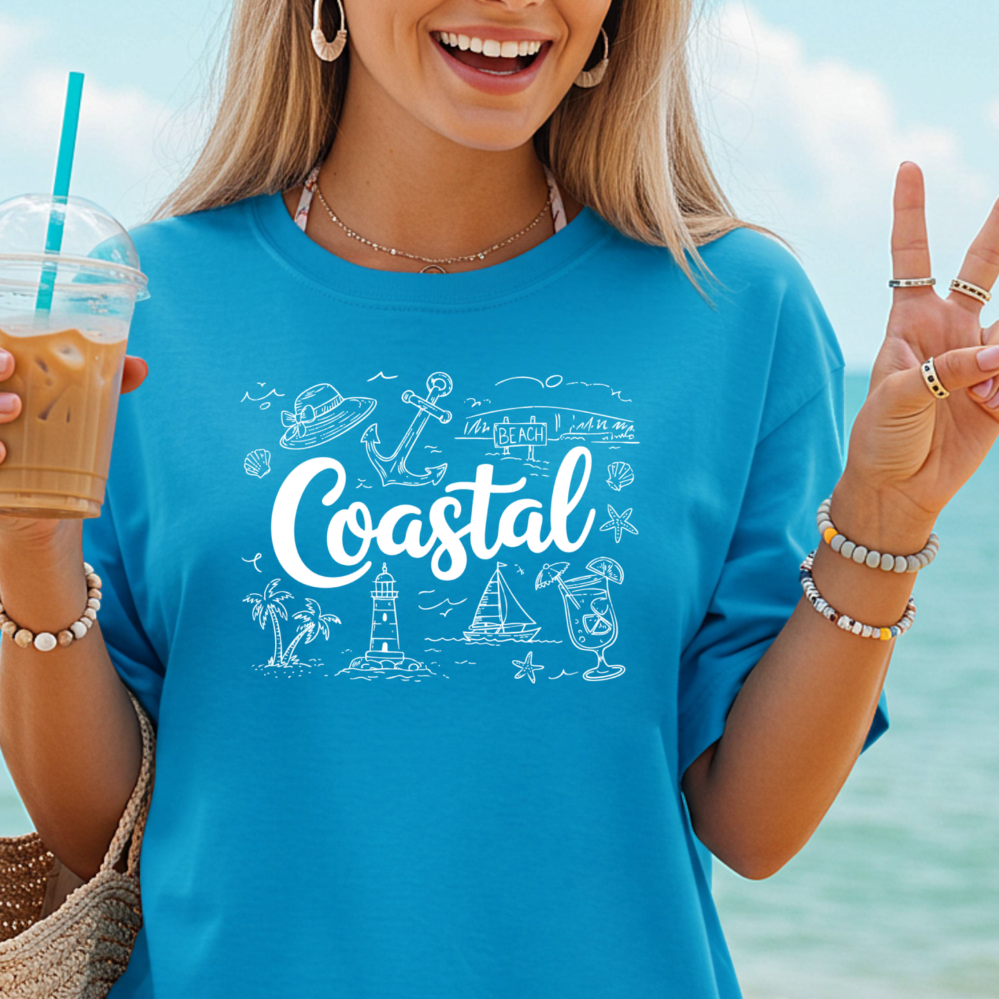 Woman wearing a blue sapphire t-shirt with 'Coastal' design by the beach