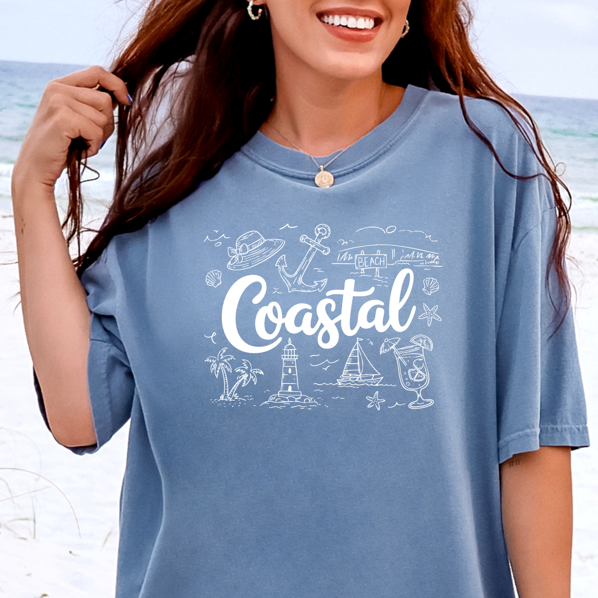 Woman wearing a blue jean t-shirt with 'Coastal' design on a beach