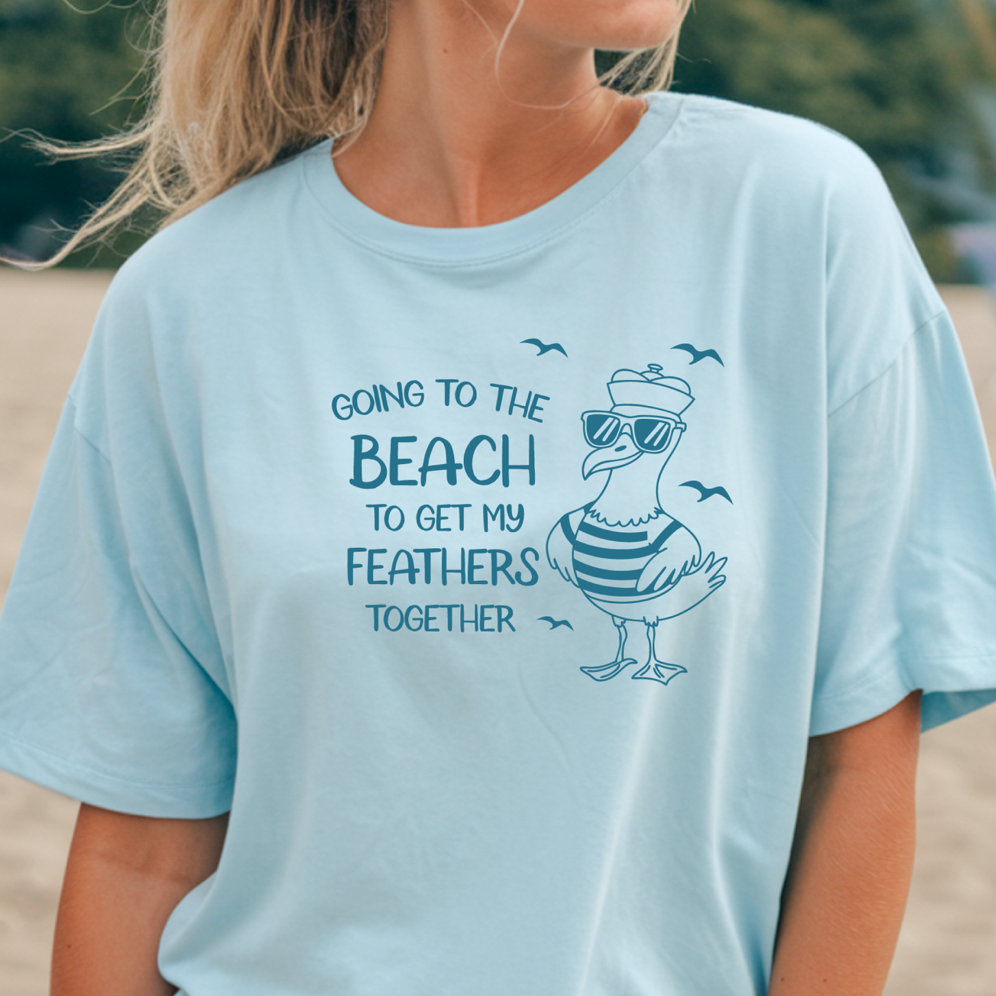 Comfort Colors t-shirt featuring a humorous blue seagull graphic wearing sunglasses and a striped shirt, beside the text “Going to the Beach to Get My Feathers Together.” Several flying birds surround the design, adding a fun coastal feel. This unisex garment-dyed tee offers a soft, vintage texture and relaxed fit, perfect for beach lovers, ocean fans, and anyone who enjoys playful summer graphic shirts.