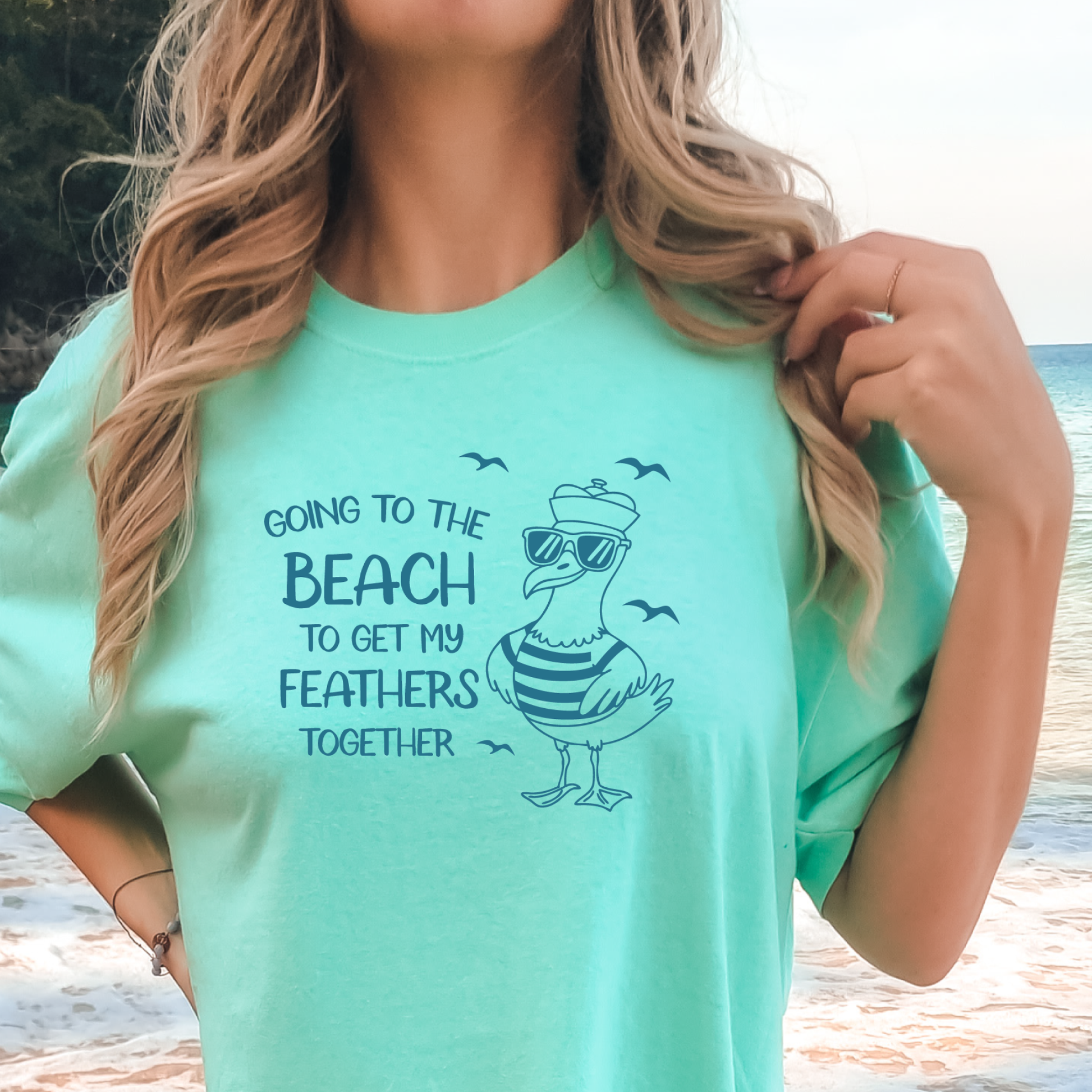 Comfort Colors t-shirt featuring a humorous blue seagull graphic wearing sunglasses and a striped shirt, beside the text “Going to the Beach to Get My Feathers Together.” Several flying birds surround the design, adding a fun coastal feel. This unisex garment-dyed tee offers a soft, vintage texture and relaxed fit, perfect for beach lovers, ocean fans, and anyone who enjoys playful summer graphic shirts.