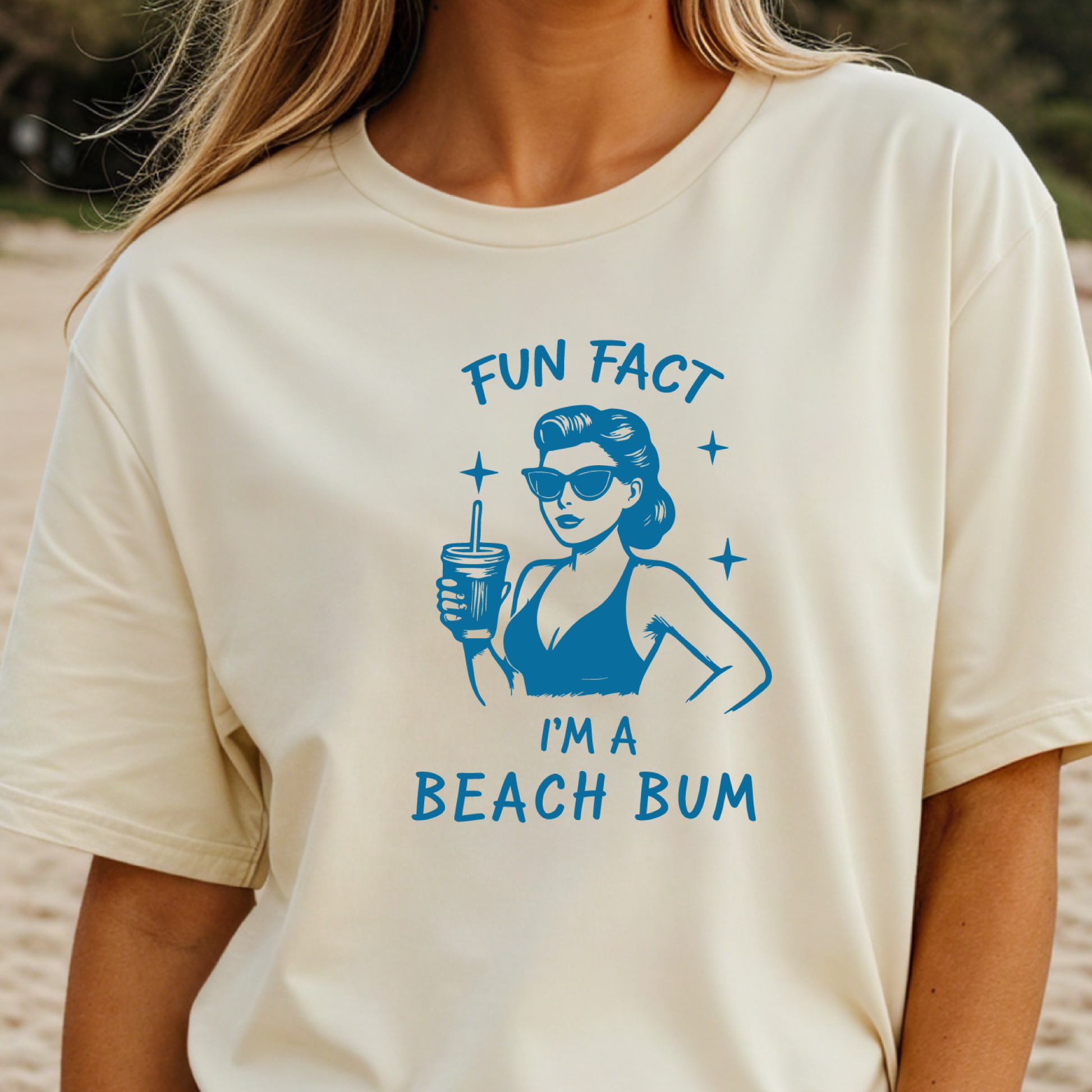 Beige t-shirt with blue graphic and text 'Fun Fact I'm a Beach Bum' worn by a person on a beach.