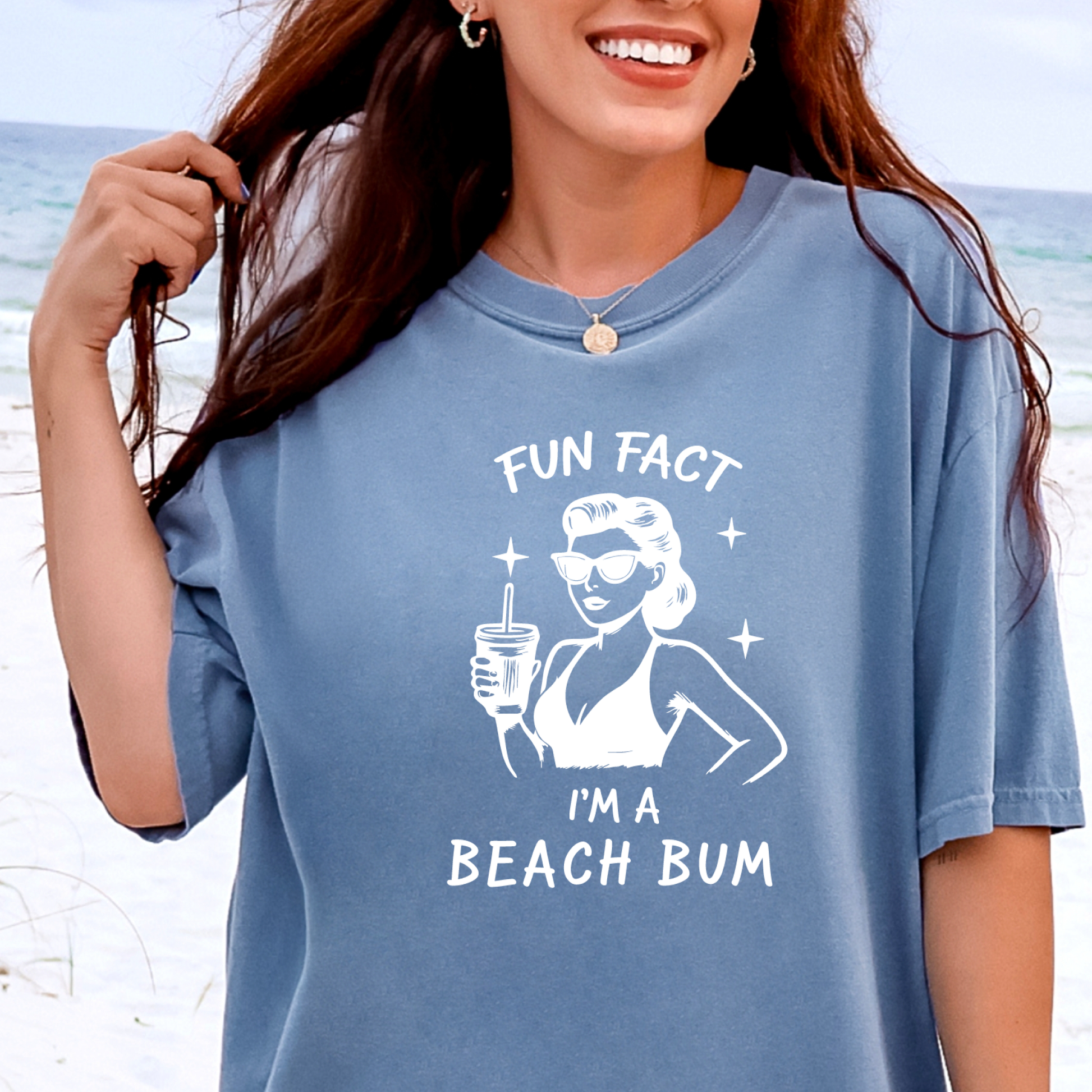 Woman wearing a blue t-shirt with a beach-themed graphic and text on a beach background