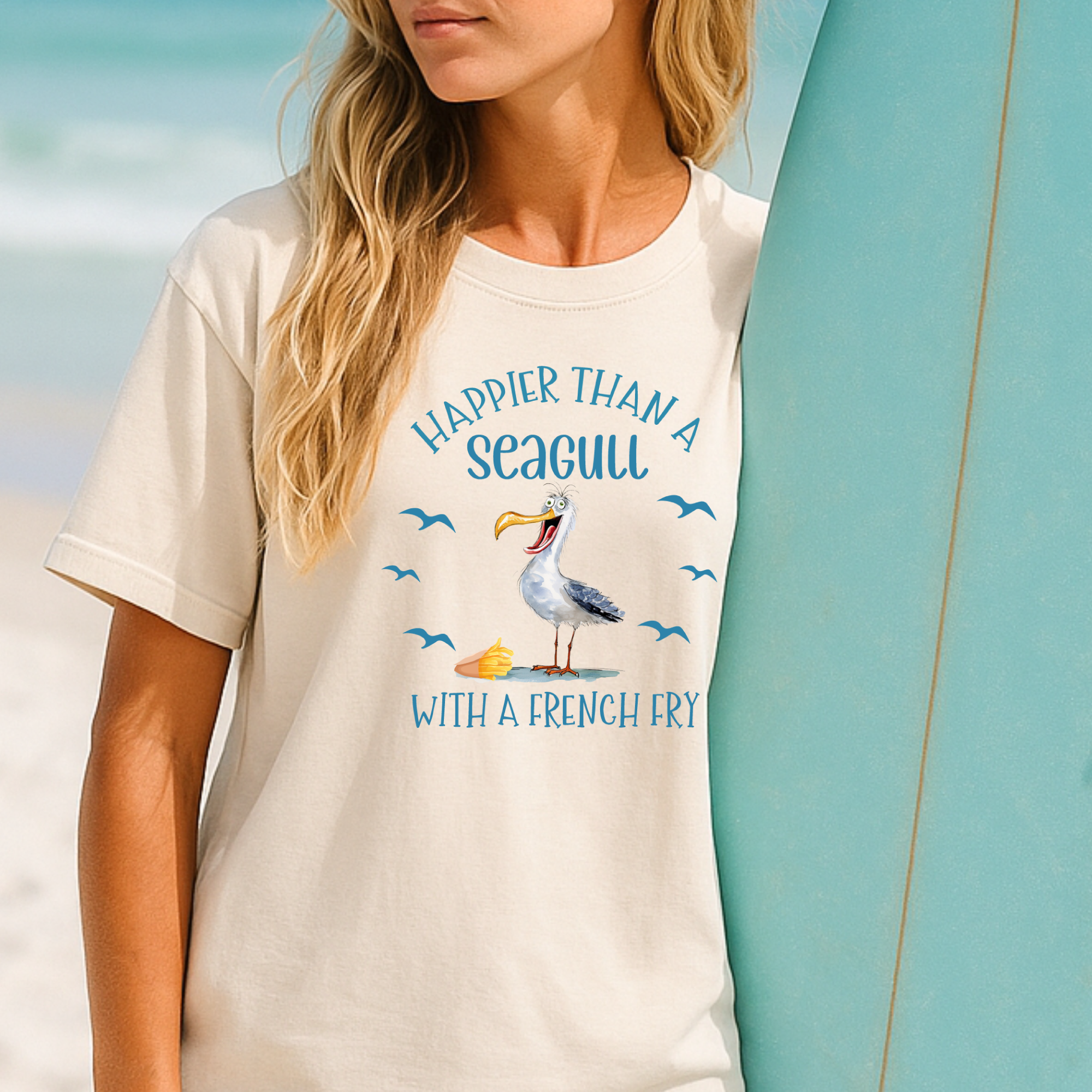 Person wearing a t-shirt with a seagull graphic and text, standing next to a surfboard.
