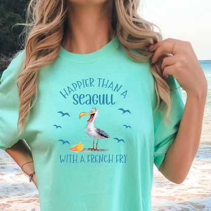 Person wearing a light green t-shirt with a seagull graphic and text at a beach.