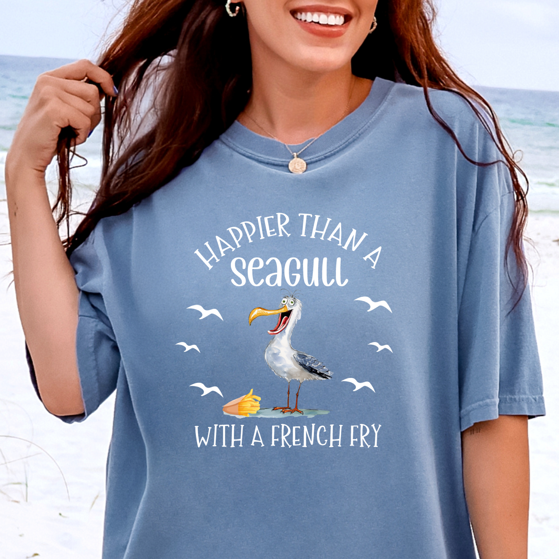 Person wearing a blue t-shirt with a seagull graphic and text on a beach background