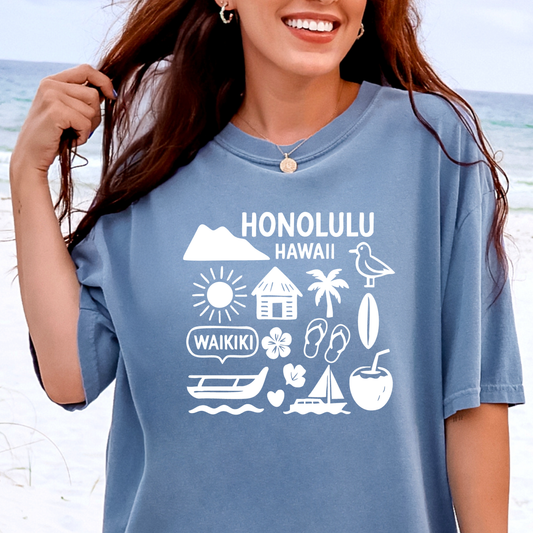 Woman wearing a blue t-shirt with Honolulu, Hawaii graphics on a beach.