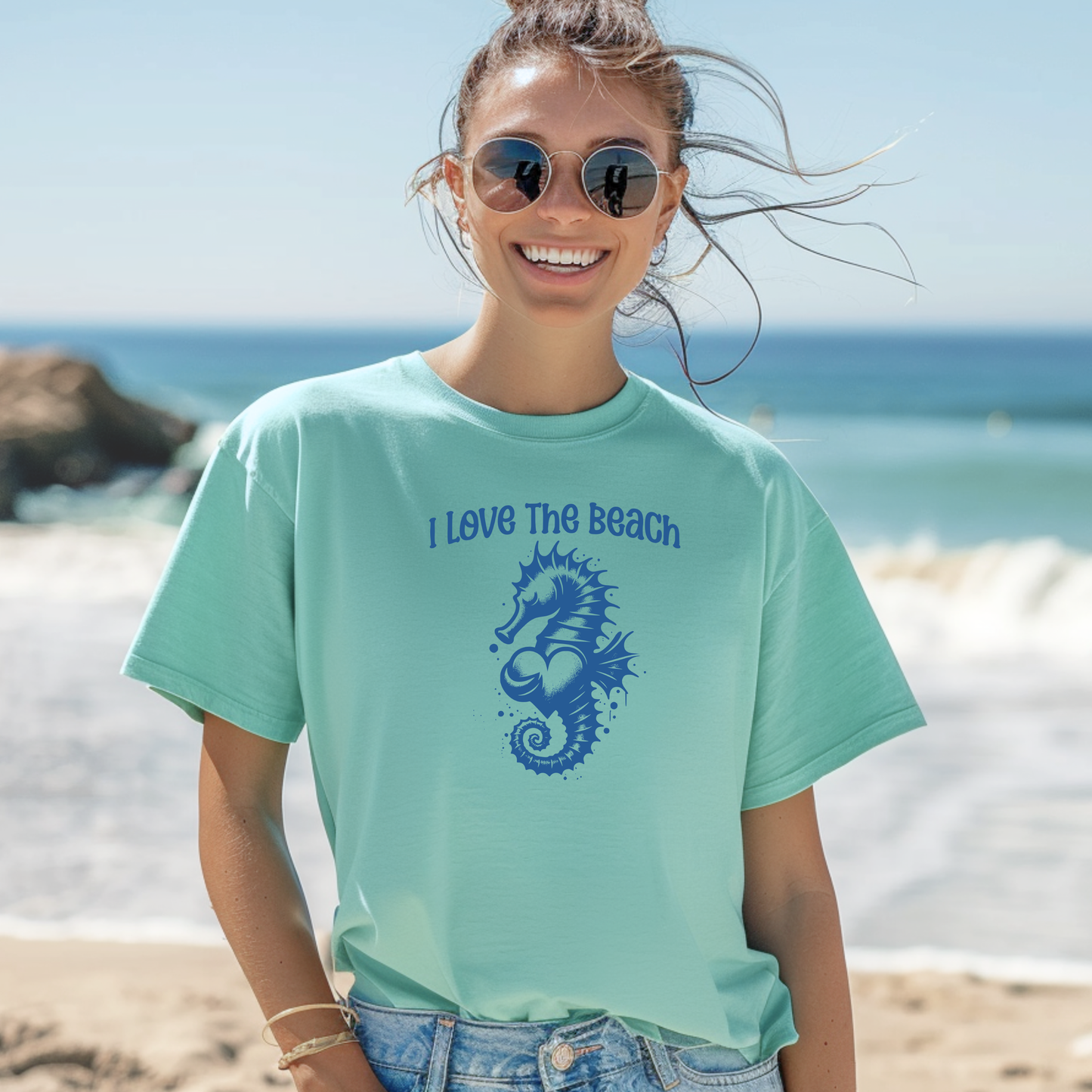Comfort Colors 1717 "I Love The Beach" t shirt with a seahorse holding a heart graphics in one color. Picture of a girl in an oversize shirt standing on the beach. 