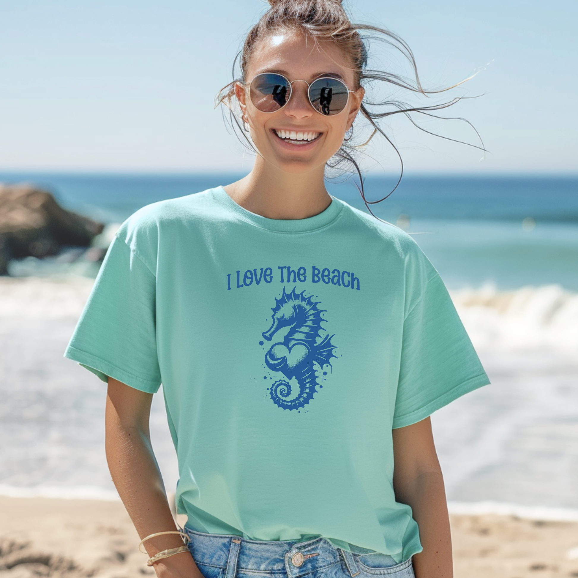 Comfort Colors 1717 "I Love The Beach" t shirt with a seahorse holding a heart graphics in one color. Picture of a girl in an oversize shirt standing on the beach. 