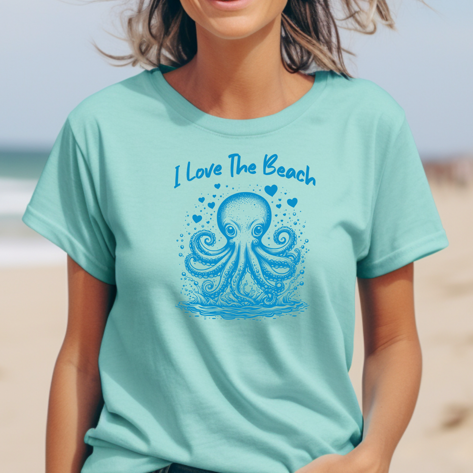 The Comfort Colors 1717 "I Love The Beach" T-shirt features a playful one-color graphic of an octopus surrounded by hearts, capturing a fun and beach-loving spirit. Worn by a girl standing on the beach, the tee embodies relaxed coastal vibes and effortless summer style, perfect for sunny days by the shore.
