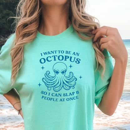 Person wearing a island reef green t-shirt with an octopus graphic and text at a beach.